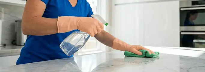 Maid service worker spraying and wiping a kitchen countertop with a microfiber cloth for sanitizing, South Bend, IN.