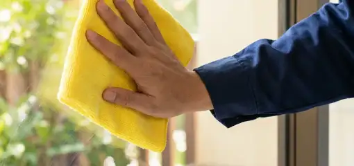 House cleaner wiping a glass window with a yellow microfiber cloth for streak-free cleaning, South Bend, IN.